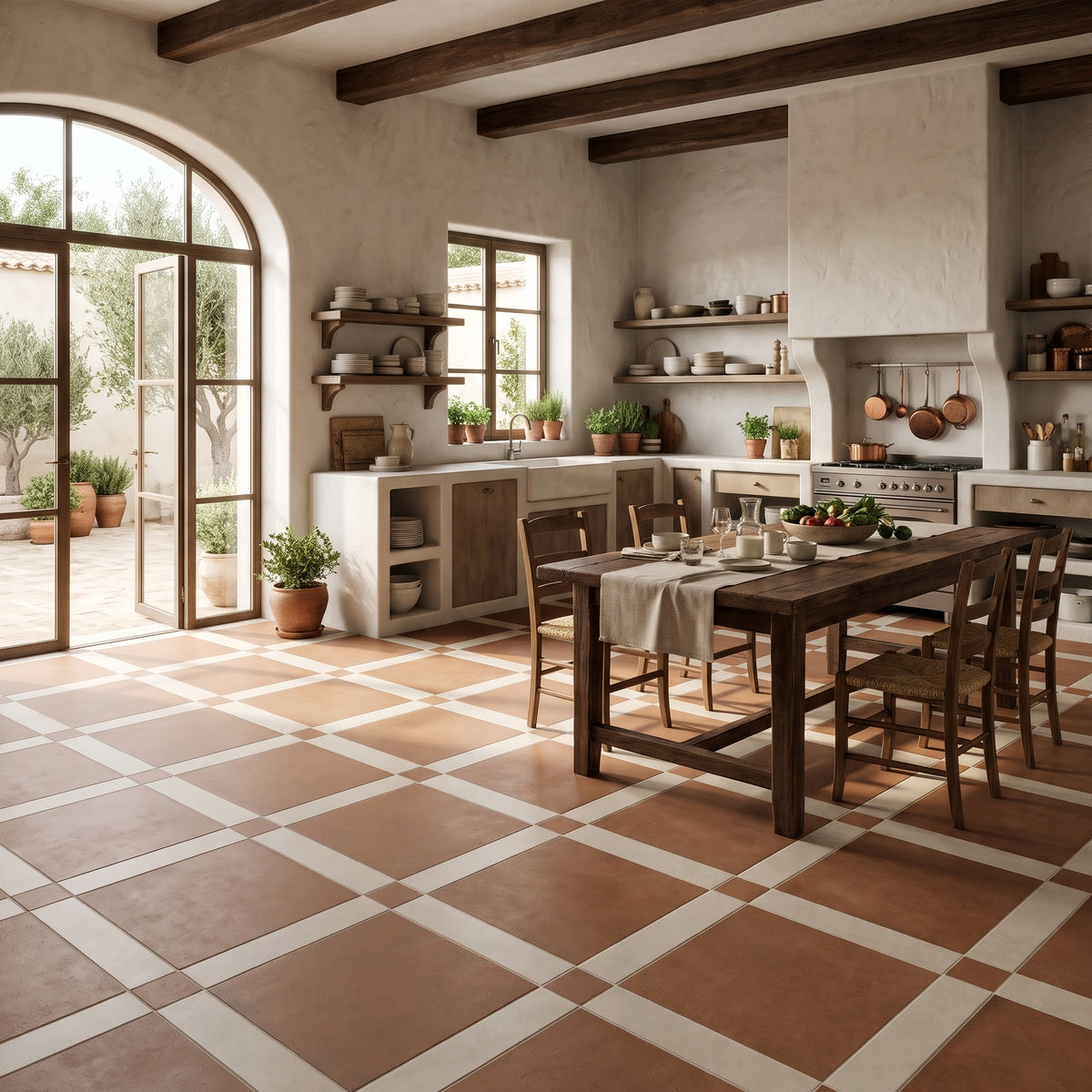 A rustic kitchen and dining room interior with terracotta and cream checkered floor tiles, a dark wood dining table with chairs, cream stucco walls, exposed dark wood ceiling beams, and large arched glass doors opening to a garden patio.