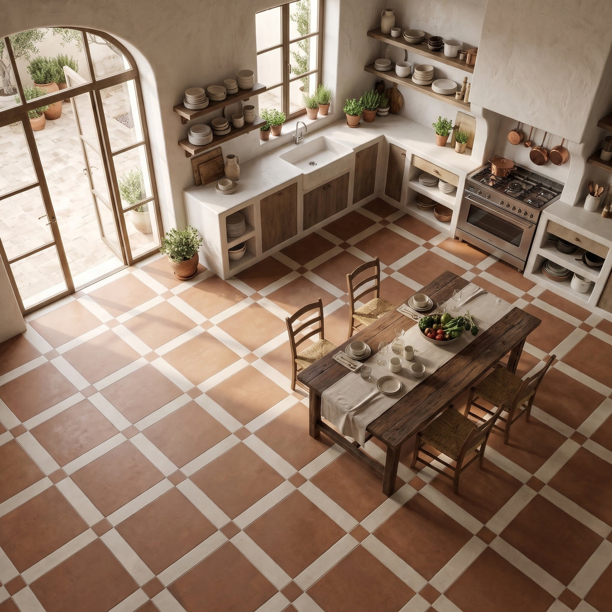 An overhead view of a rustic kitchen featuring terracotta and cream checkered floor tiles, a wooden dining table with four chairs, white countertops, and a stainless steel gas stove.