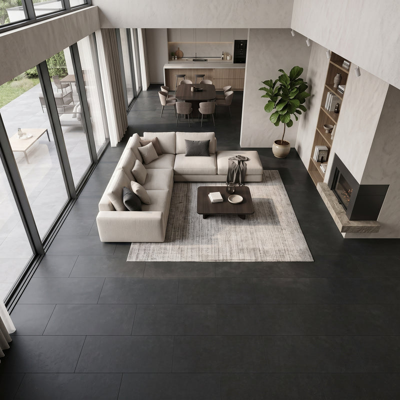 An overhead view of a modern living room featuring a light beige sectional sofa arranged around a dark wood coffee table on a textured light gray rug. The room has dark charcoal tiled flooring, large floor-to-ceiling windows, a built-in fireplace, and a dining area in the background.