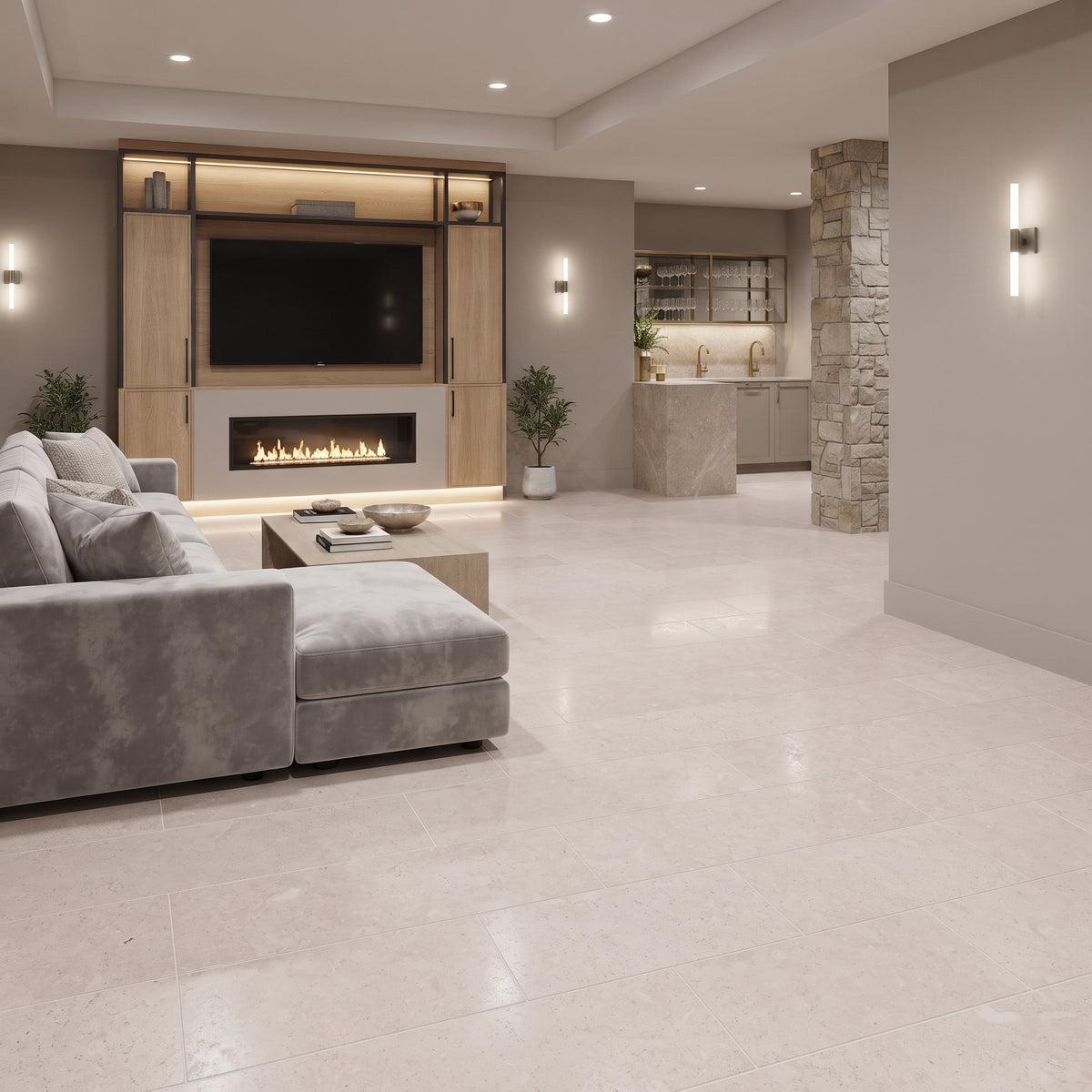 A modern open-concept living room with large light beige stone floor tiles, a gray sectional sofa, a built-in wood TV wall with a fireplace, and a stone column in the background.