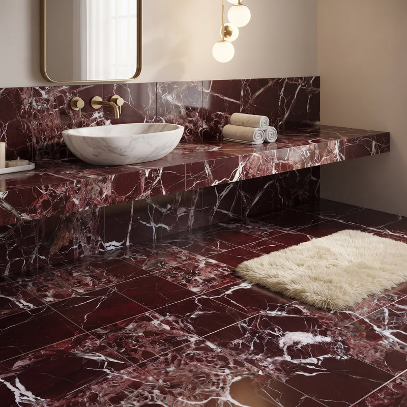 A luxury bathroom featuring deep burgundy marble tiles on the floor and floating vanity countertop, with a white marble vessel sink, gold fixtures, a cream shag rug, and a wall mirror.