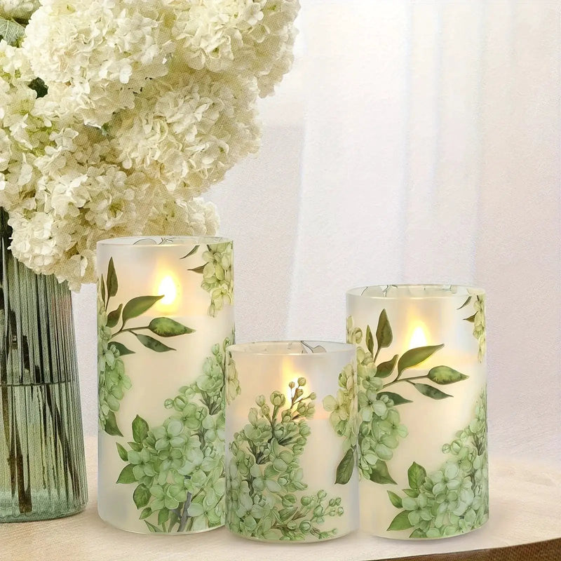 A set of 3 flameless candles, flickering LED pillar candles, with a 10-button remote control. They feature a green floral theme, are suitable for spring and summer, and can be used on the dining tables at wedding venues by House Of Avana