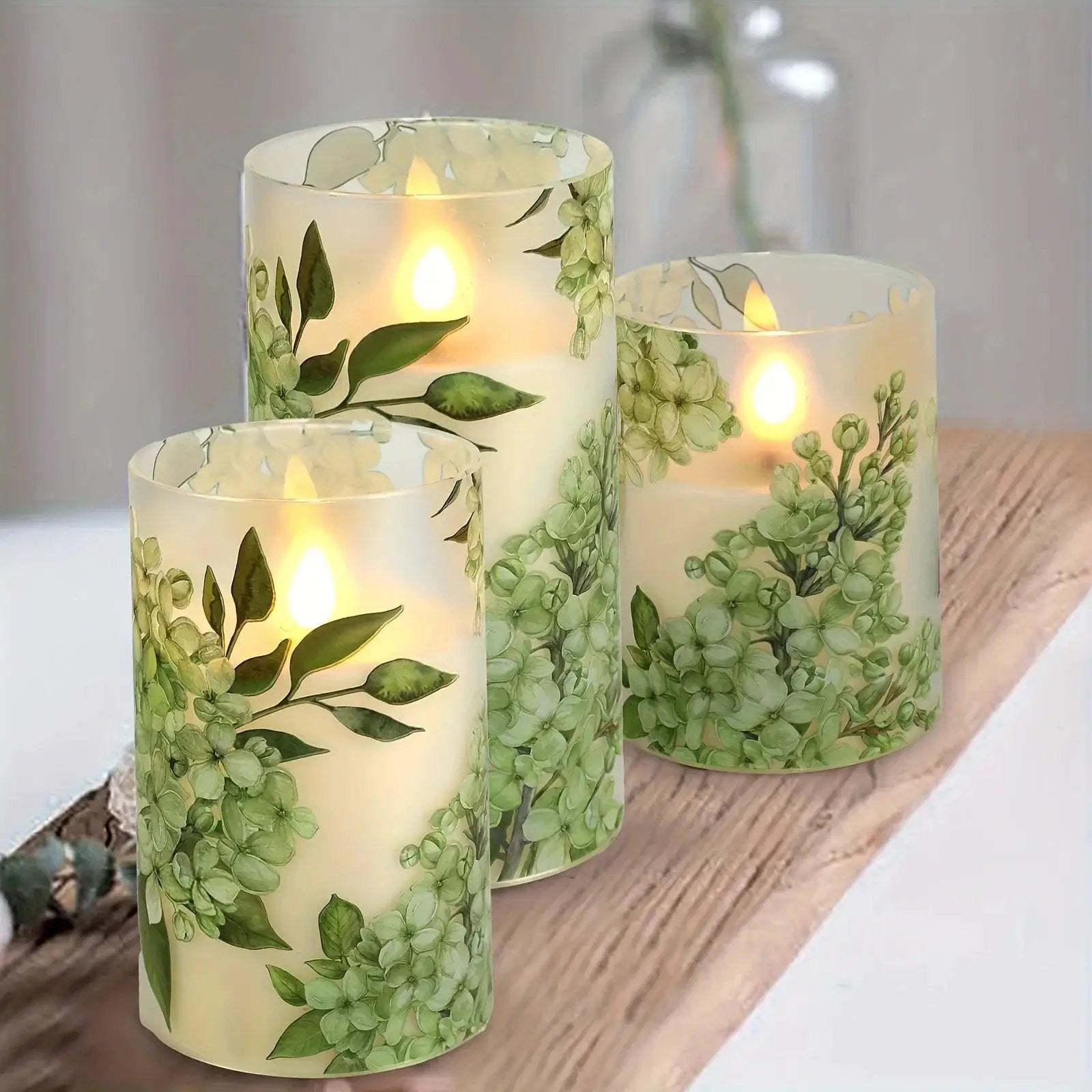 A set of 3 flameless candles, flickering LED pillar candles, with a 10-button remote control. They feature a green floral theme, are suitable for spring and summer, and can be used on the dining tables at wedding venues by House Of Avana