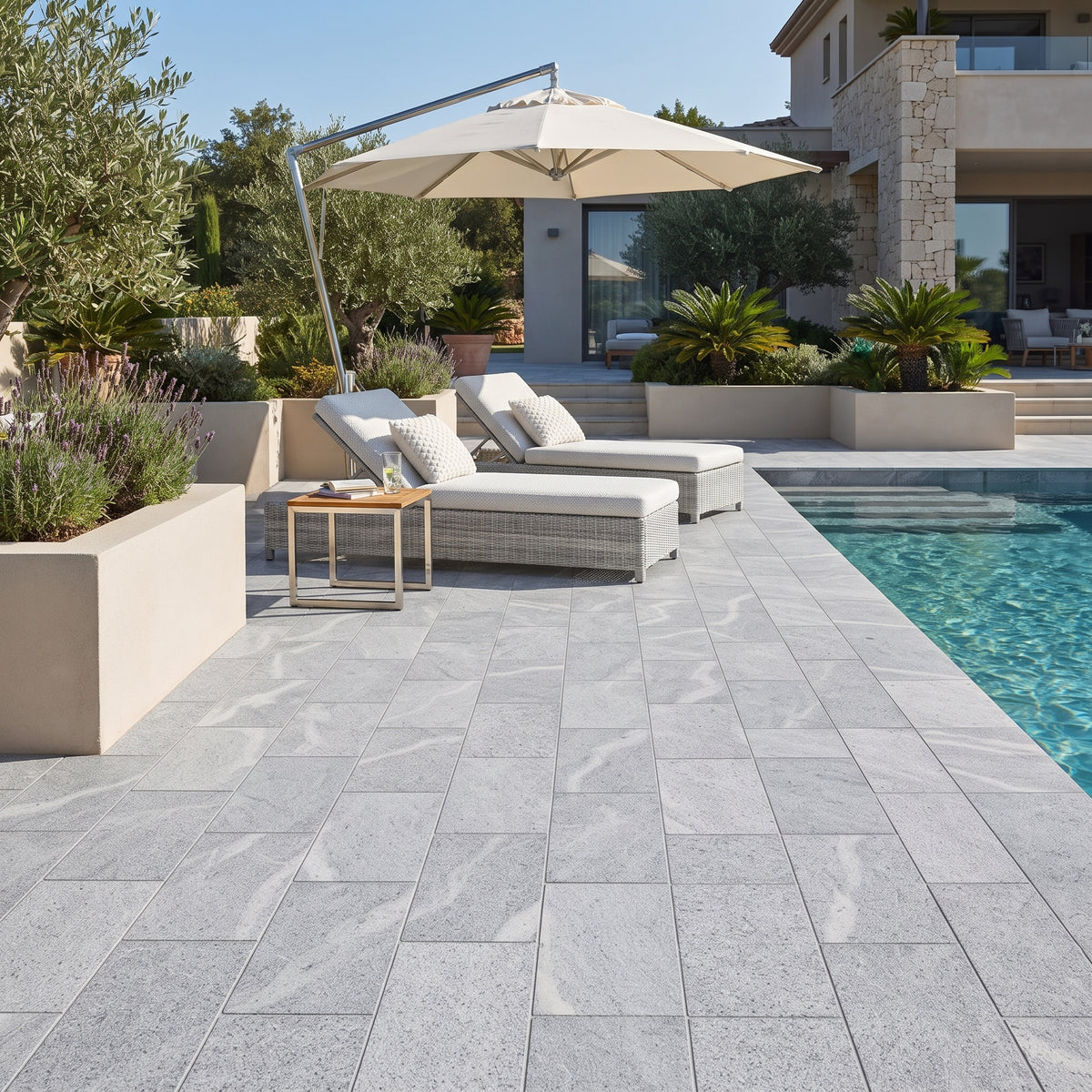 Light gray stone pavers with natural marble-like veining arranged around a swimming pool, with outdoor lounge chairs, a large patio umbrella, and a modern villa in the background.