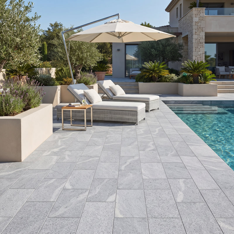 Light gray stone pavers with natural marble-like veining arranged around a swimming pool, with outdoor lounge chairs, a large patio umbrella, and a modern villa in the background.