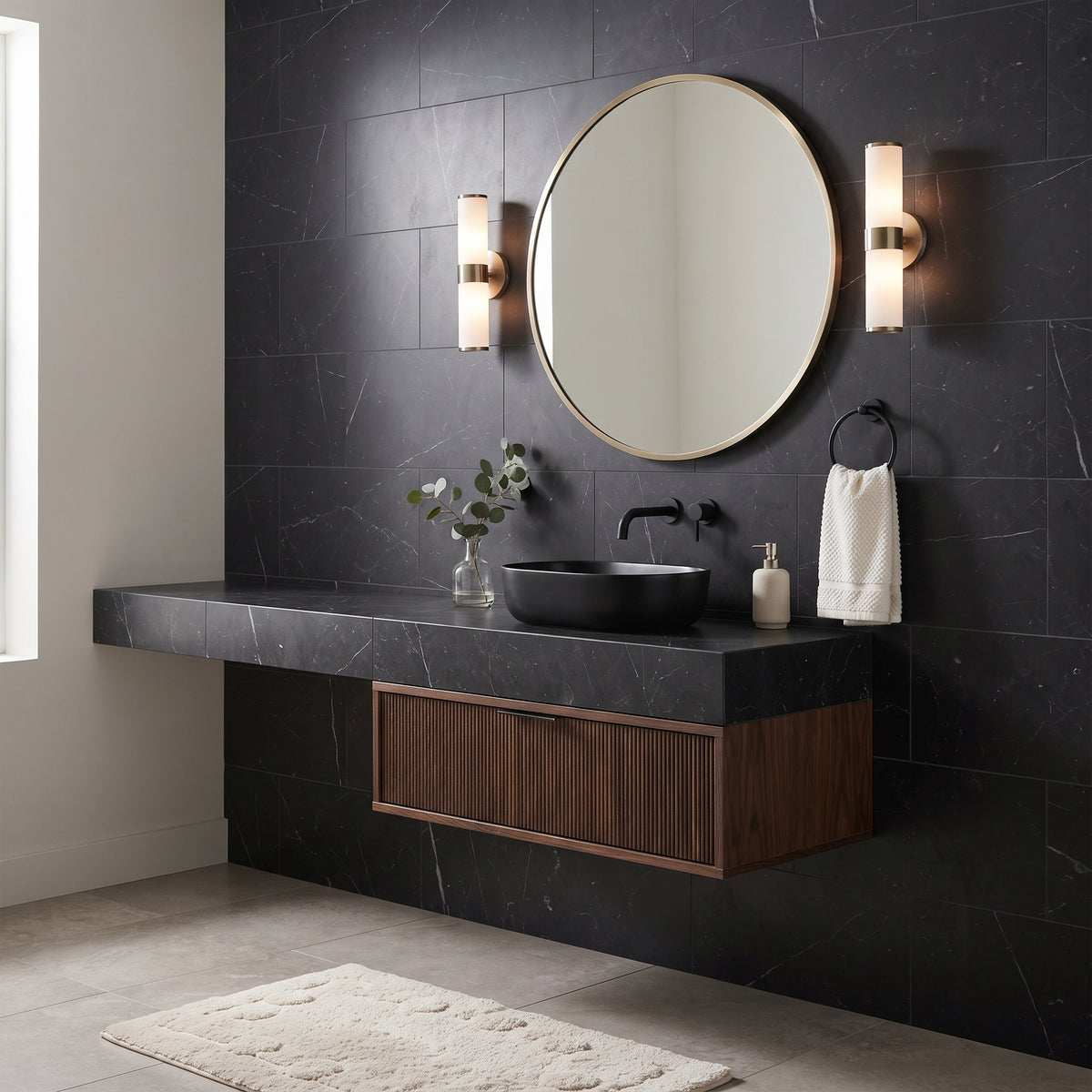 Modern floating bathroom vanity with a black stone countertop and sink, dark wood cabinet, round wall mirror, and matching sconces against a black tiled wall.