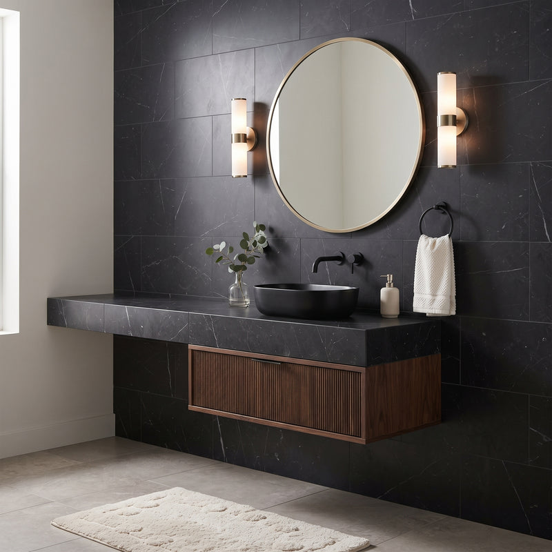 Modern floating bathroom vanity with a black stone countertop and sink, dark wood cabinet, round wall mirror, and matching sconces against a black tiled wall.