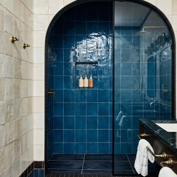 Arched walk-in shower clad in glossy blue zellige tile
