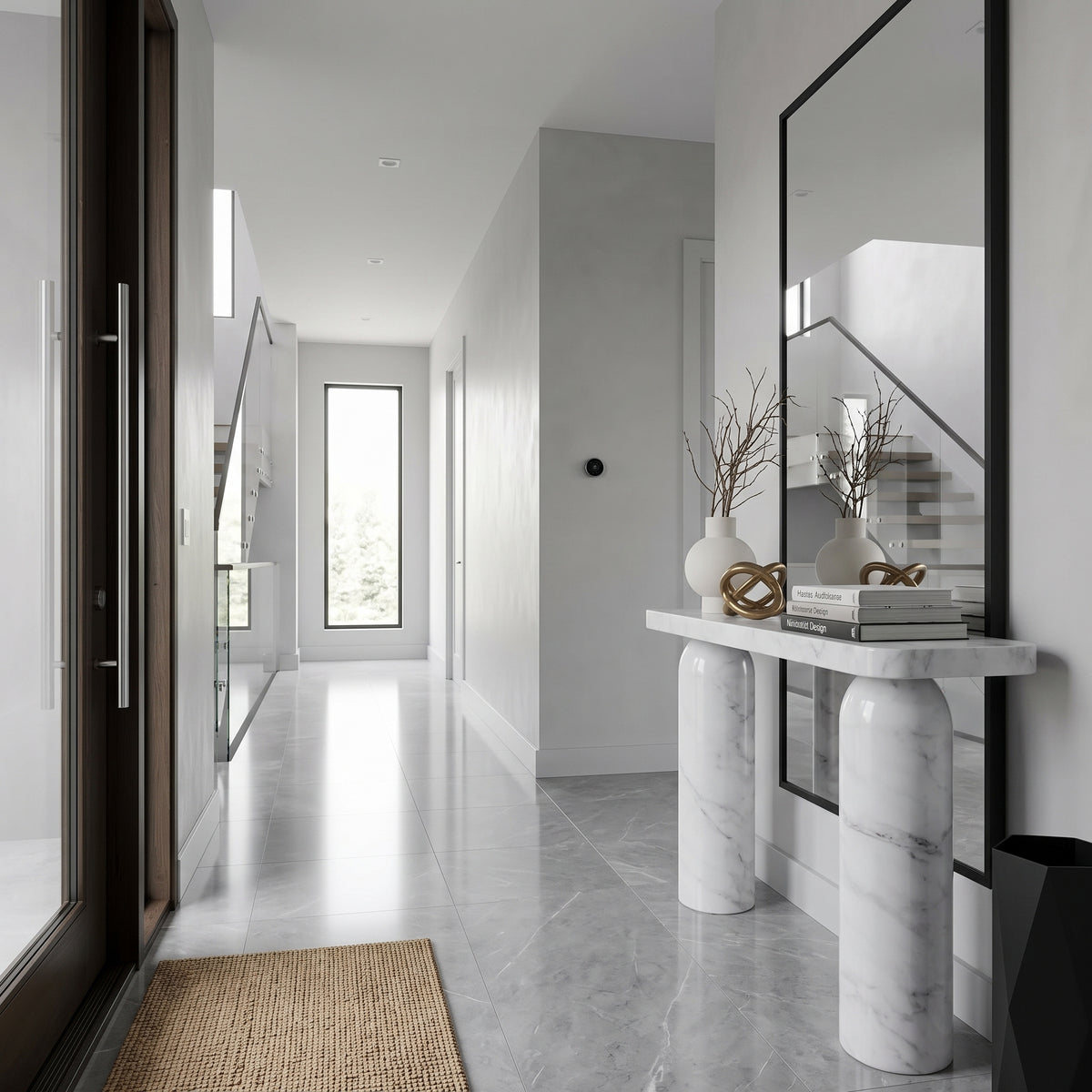 A modern entryway console table with cylindrical marble legs and a white marble top, styled with vases, books, and a mirror in a bright, minimalist hallway.