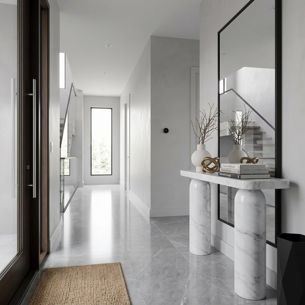 A modern entryway console table with cylindrical marble legs and a white marble top, styled with vases, books, and a mirror in a bright, minimalist hallway.