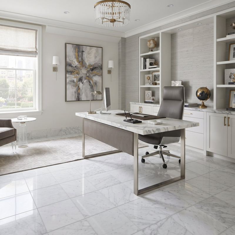 A modern home office featuring a large desk with a white marble top and brushed steel frame, paired with a dark gray leather office chair. The room has light gray marble floors, white built-in shelves, and a large abstract painting on the wall.