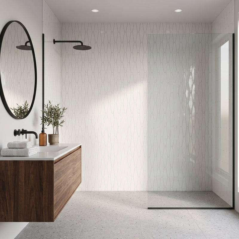 Modern bathroom interior with a glass shower door, white patterned wall tile, floating wood vanity, black faucet, round mirror, and light stone floor.