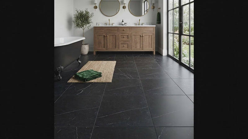 Elegant modern bathroom featuring large-format black honed marble floor tiles with subtle white veining, a wood vanity, freestanding bathtub, and brass fixtures.