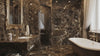 Luxury bathroom featuring dark brown marble walls and floor, a white clawfoot bathtub, a double vanity with a large ornate gold mirror, and a crystal chandelier.