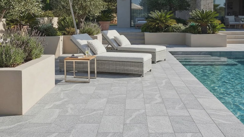Light gray stone pavers with natural marble-like veining arranged around a swimming pool, with outdoor lounge chairs, a large patio umbrella, and a modern villa in the background.