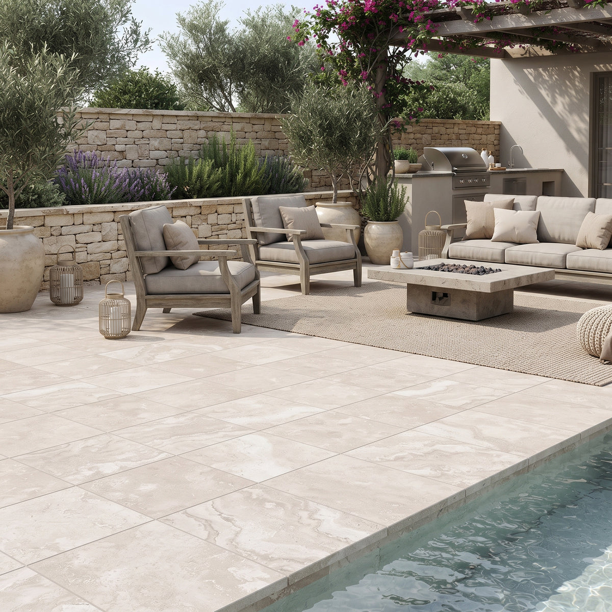 Large-format light beige stone-look pool deck tiles installed in a luxurious outdoor patio setting with a swimming pool, modern lounge chairs, a coffee table, and a stone wall backdrop.